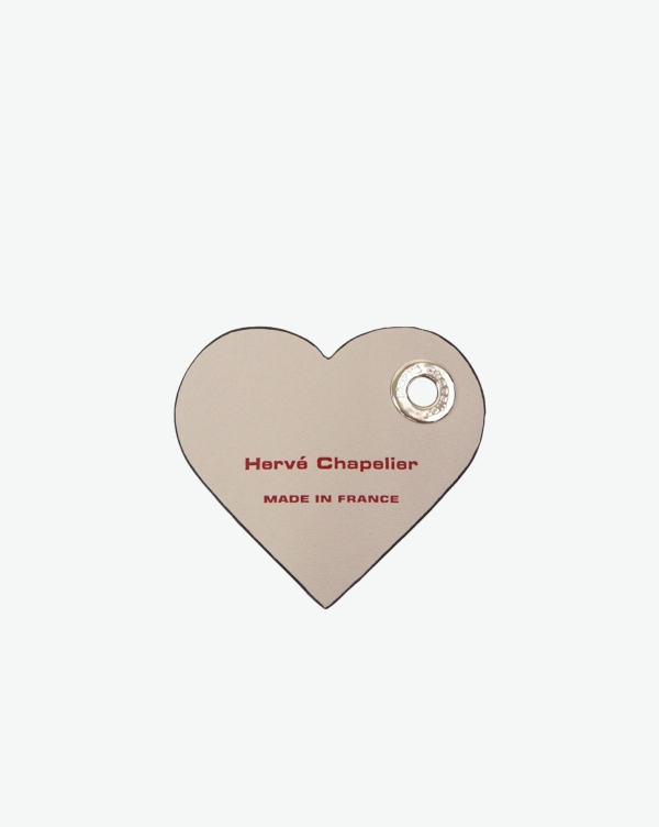 Hervé Chapelier -  - "Packshot of a 122L flat charm
in the shape of a heart with the Hervé Chapelier logo.
The charm is made of leather with a eyelet in the middle in a XXS size.
Charme en forme de coeur en cuir dans une taille XXS"